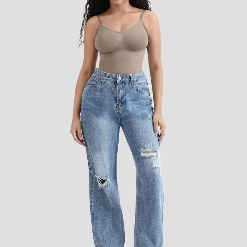 Person wearing a beige tank top and blue jeans on a light gray background