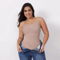 Woman wearing a beige tank top and blue jeans against a white background